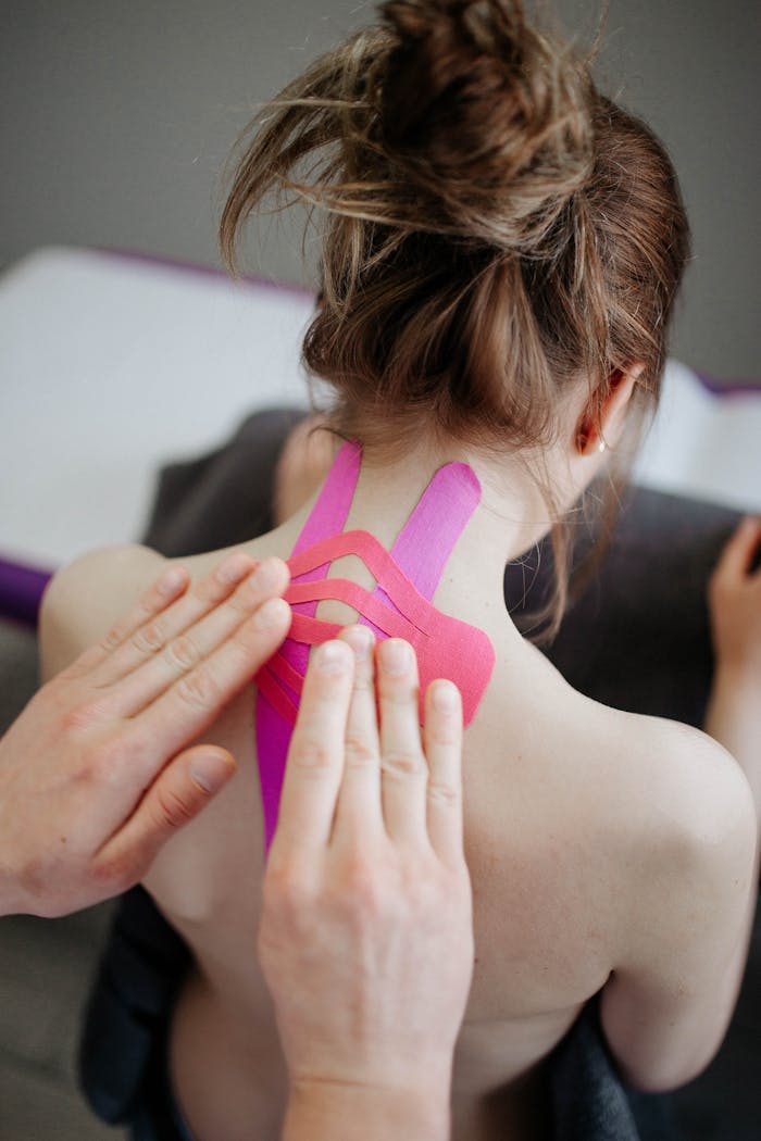 Close-up of hands applying kinesio tape on a woman's neck for pain relief.